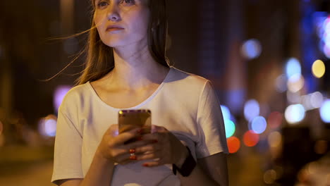 A-young-woman-at-night-in-the-city-calls-a-taxi-through-a-smartphone-while-looking-into-the-screen-of-a-mobile-phone-and-pointing-out-the-coordinates-and-address-of-the-trip.